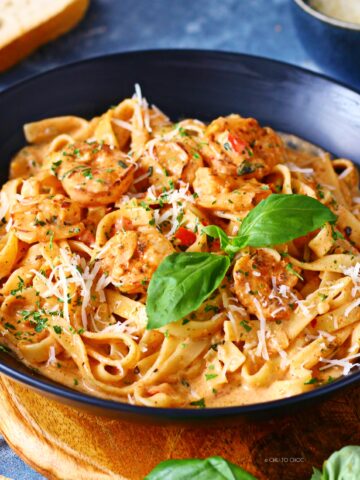 Creamy Cajun shrimp pasta in a black dish garnished with fresh basil, dried parsley and grated Parmesan.