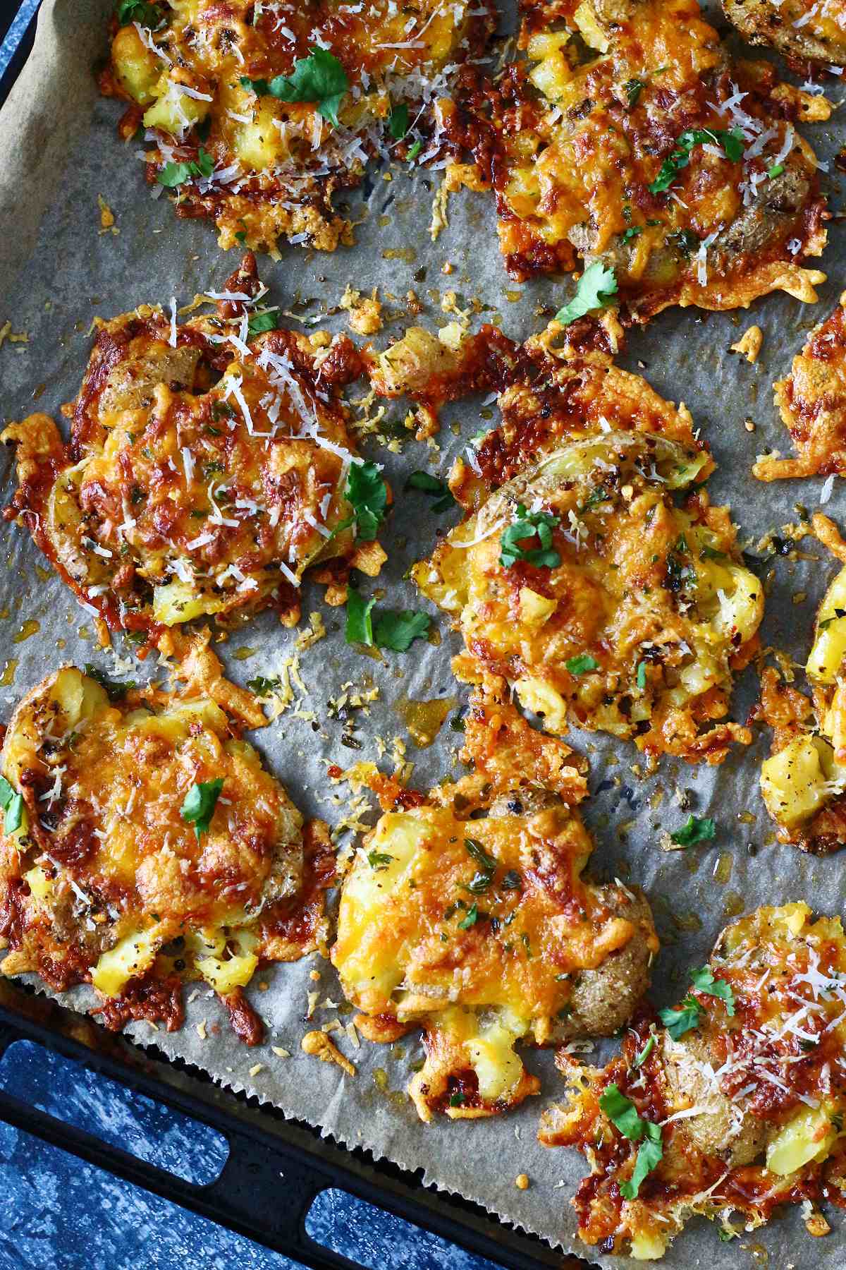 Cheesy smashed potatoes on a parchment paper, garnished with chopped cilantro.