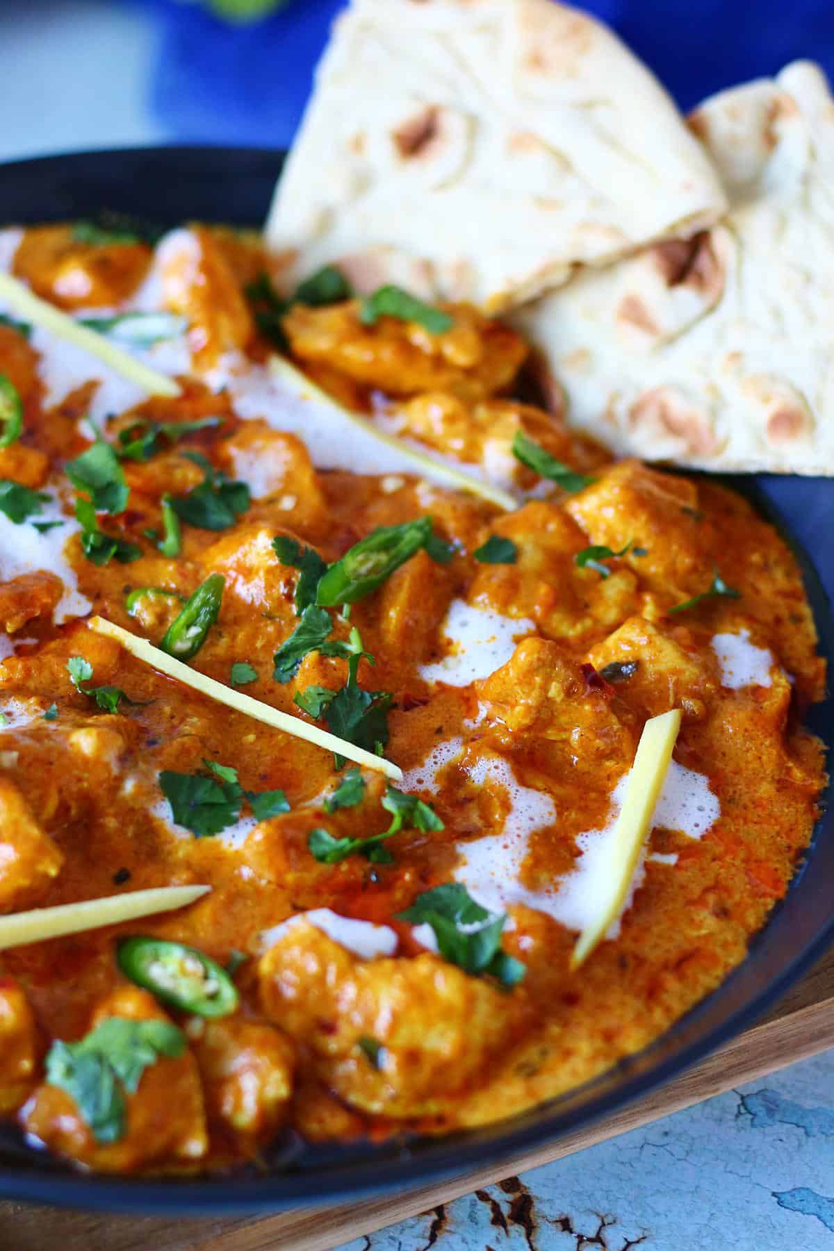 Close up of chicken handi garnished wth cream, cilantro, sliced ginger and green chilies.