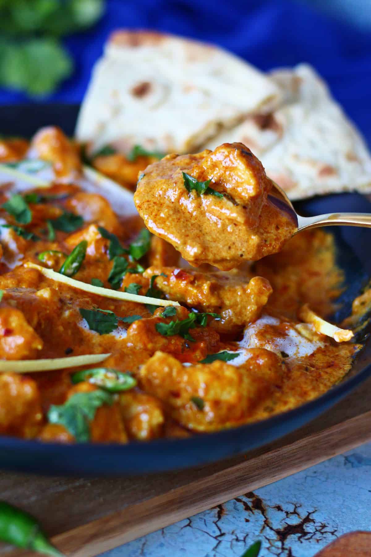 Chicken curry in a spoon with its serving plate at the back.