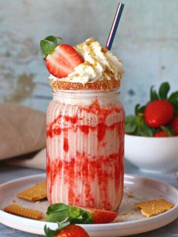 Strawberry cheesecake milkshake in a tall glass with whipped cream and a straw.