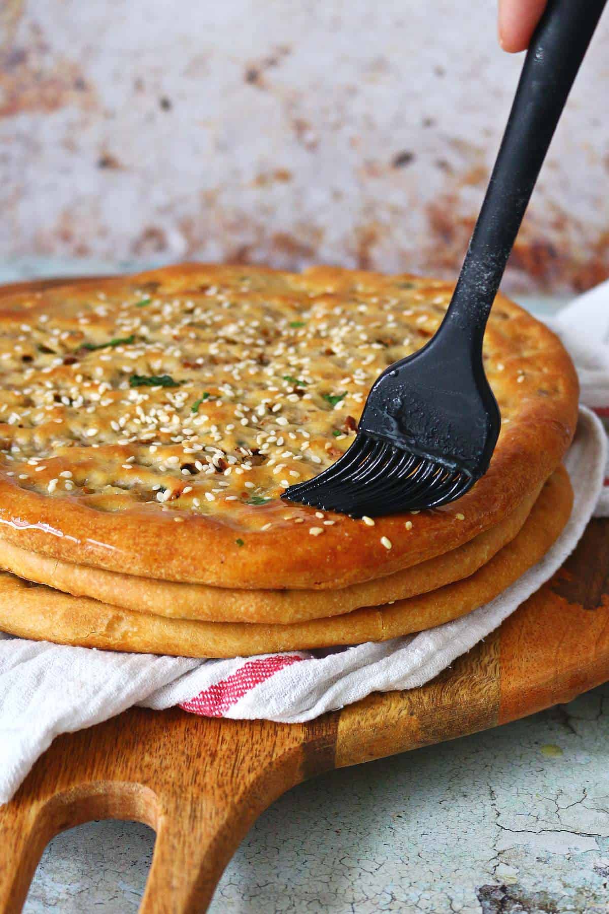 Brushing melted butter on the top naan of a stack of keema naan.