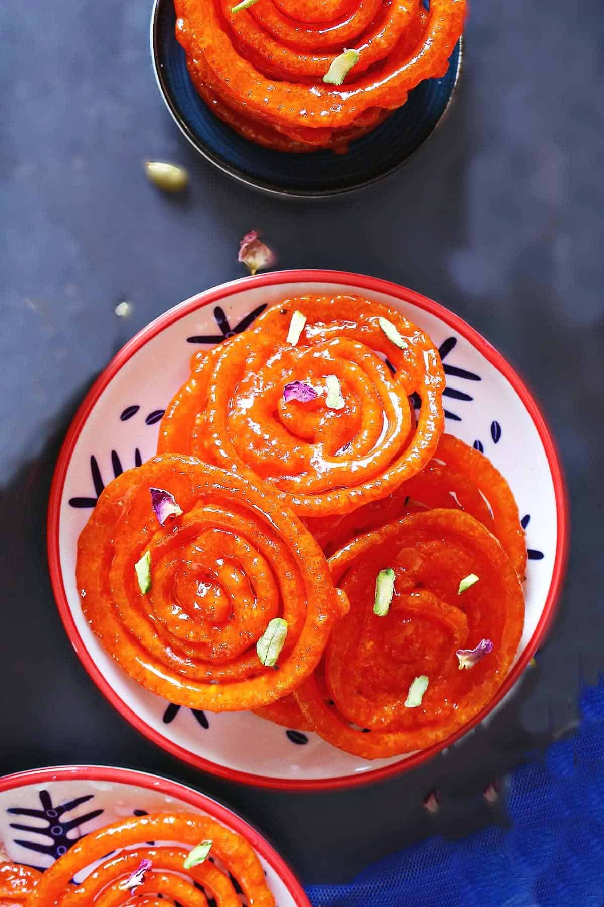 Overhead shot of jalebis in a plate garnished with rose petals and sliced pistachios.
