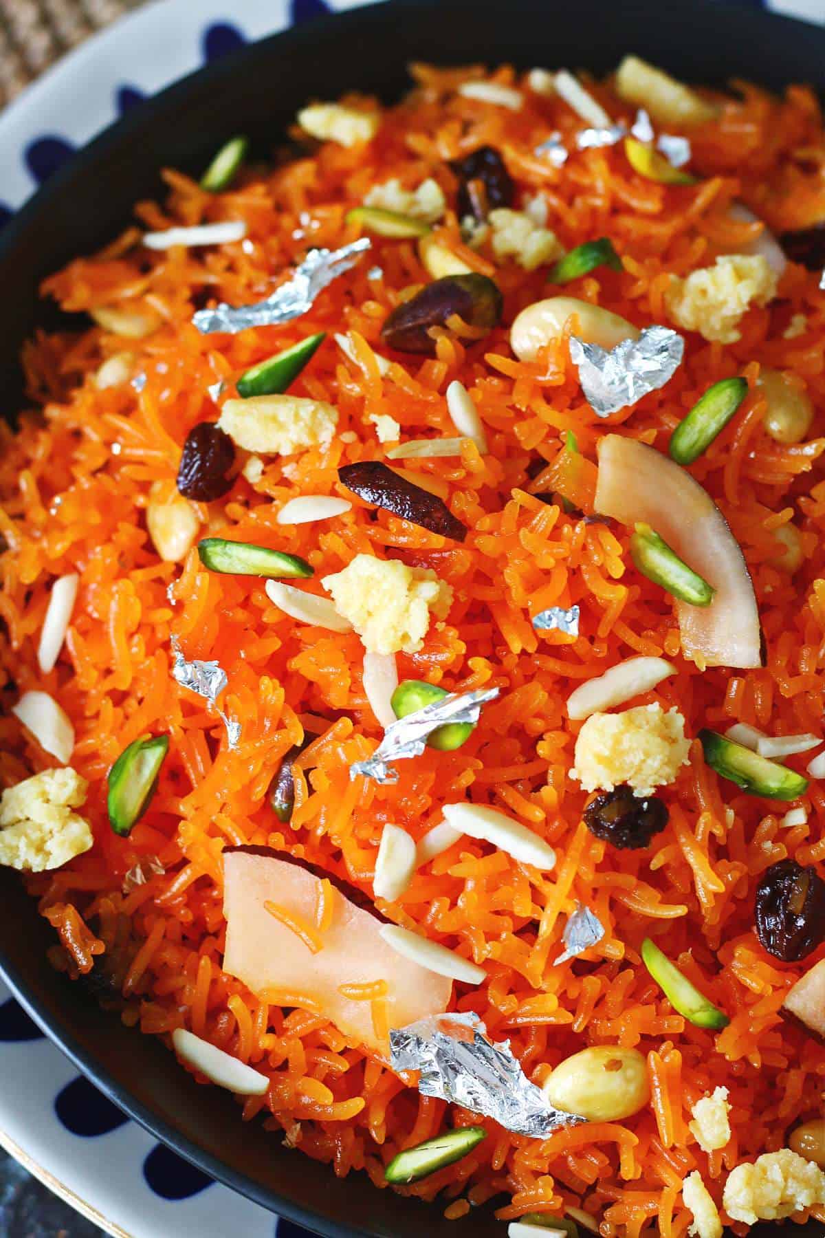 Close up of orange rice garnished with almonds, pistachios, dried coconut and silver leaf.