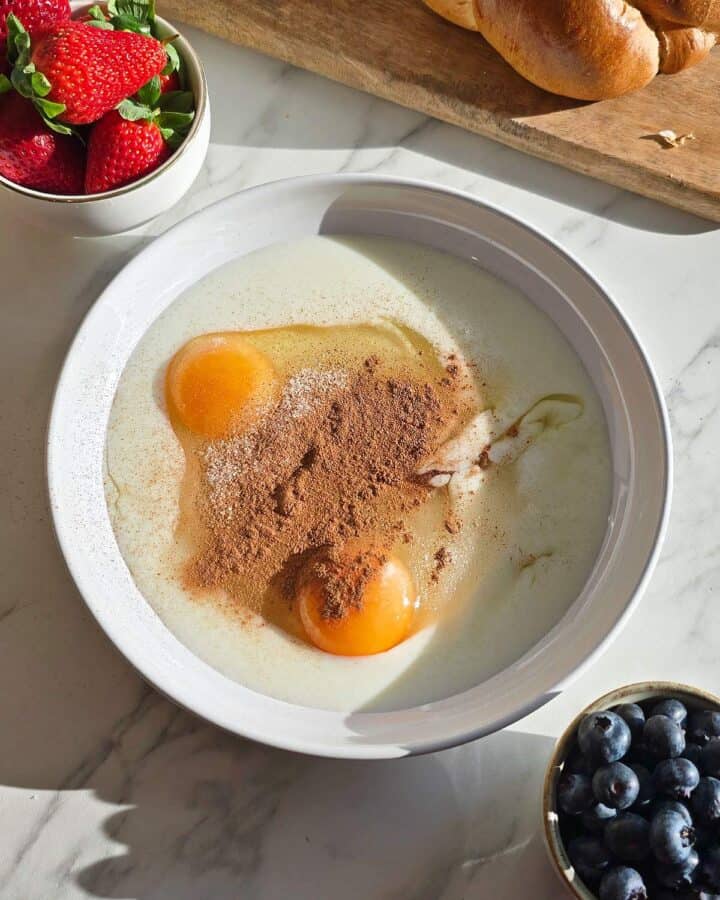 A shallow dish with two eggs, buttermilk, sugar and cinnamon powder.