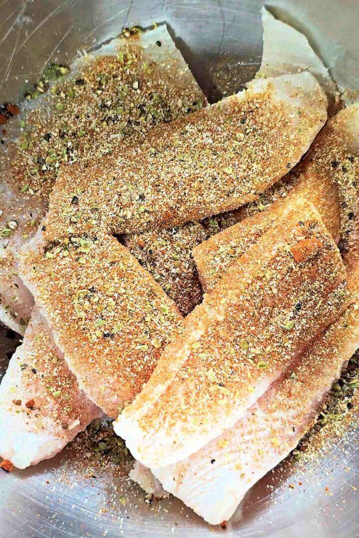 Raw fish fillets with blackened seasoning in a stainless steel pot.