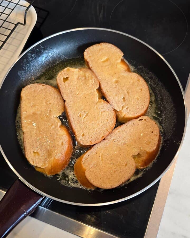 Soaked brioche slices cooking in a frying pan.