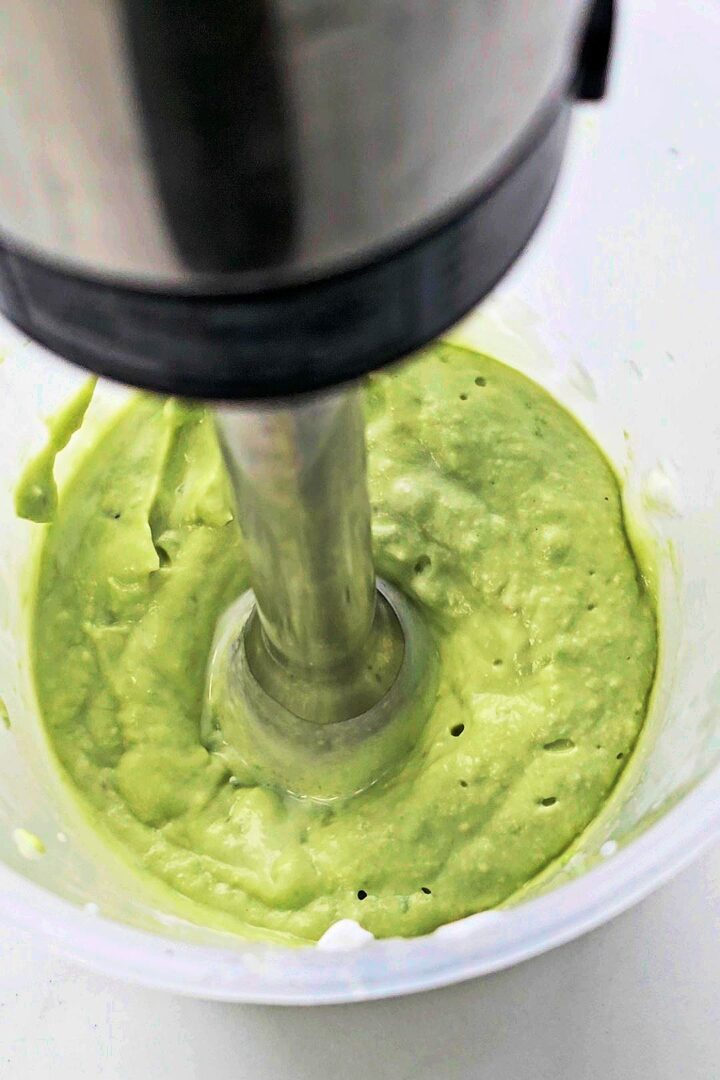 Blending avocado crema with a hand blender in a plastic jug.