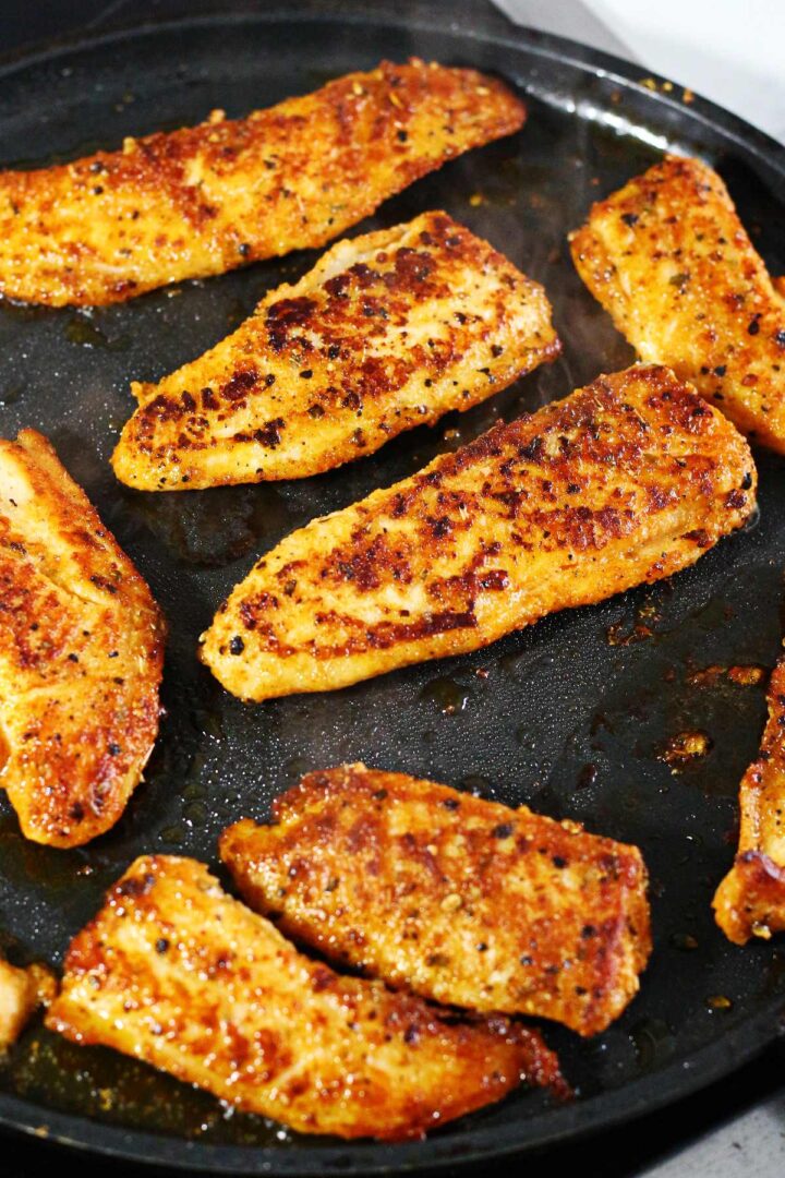 Pan-seared fish on a flat black pan.