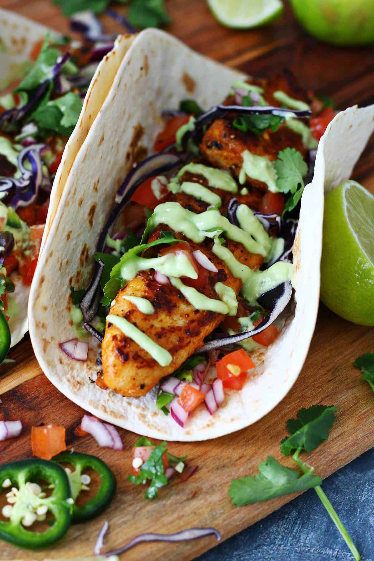 Close of fish taco on a wooden board with garnishes around it.