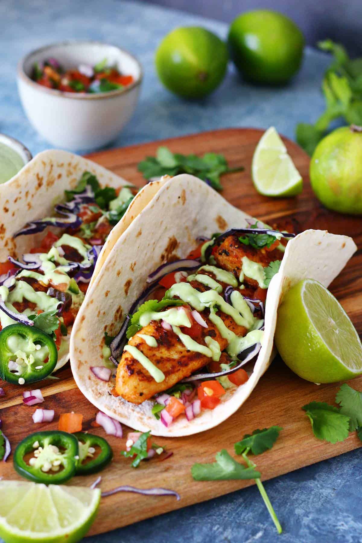 One fish taco in focus with avocado cream sauce, shredded cabbage and pico de gallo.