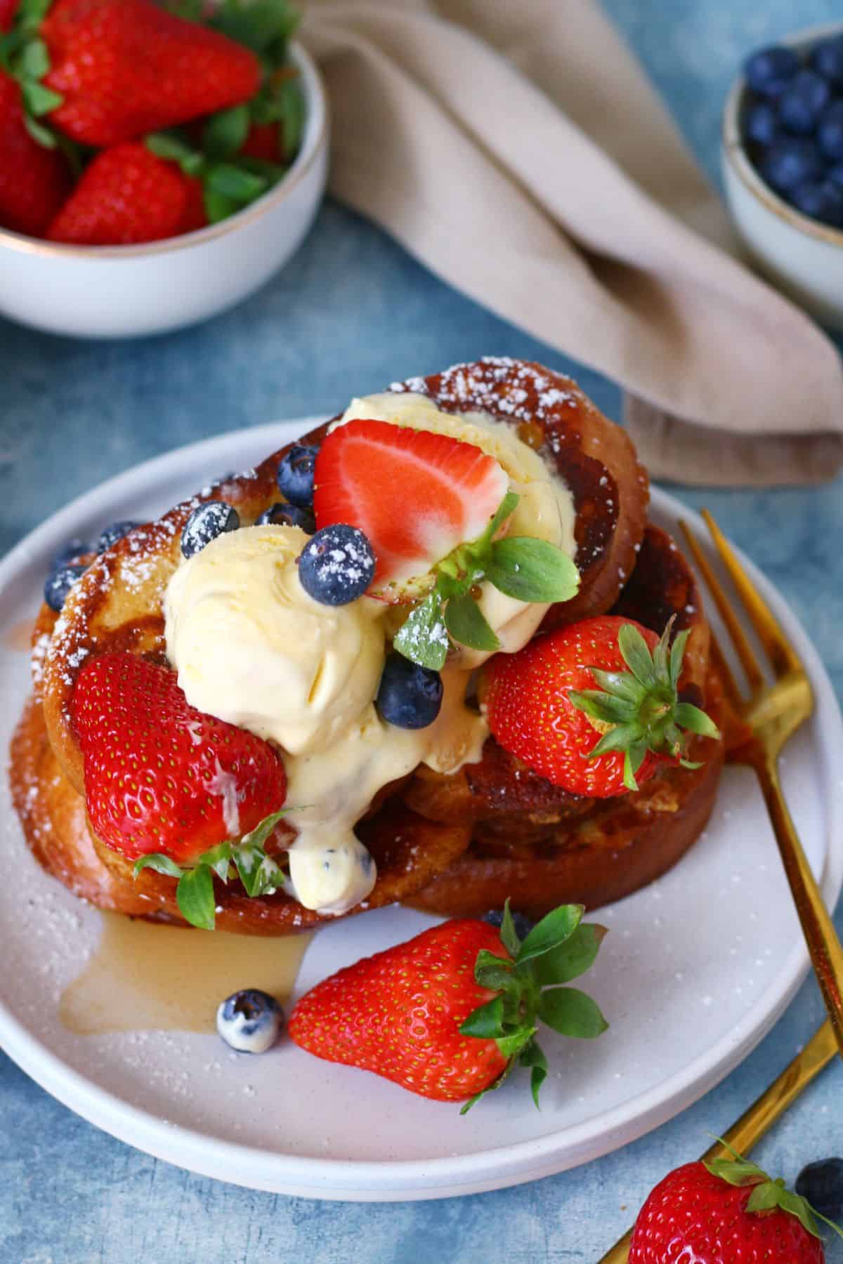 Stack of French toast in a plate with berries, vanilla ice cream and a fork on the side.