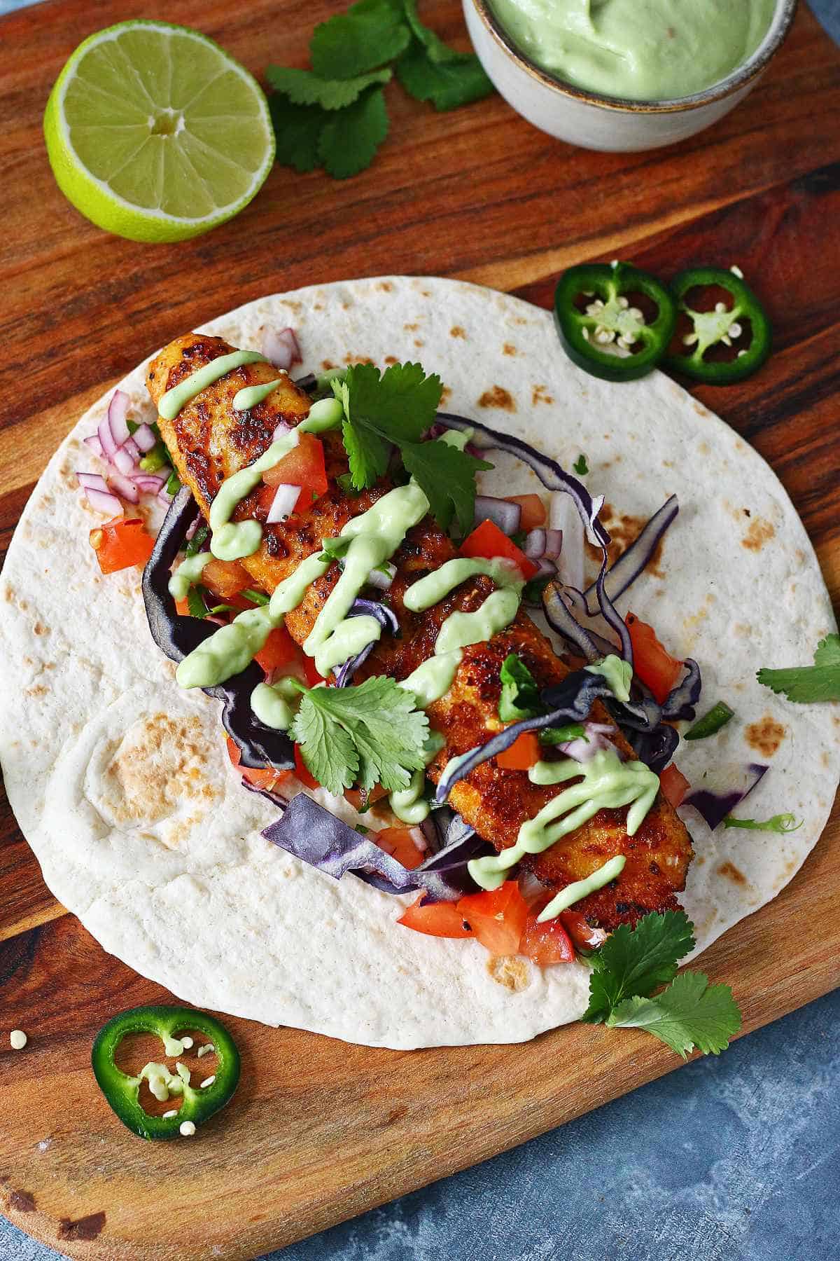 An open tortilla with blackened fish, pico de gallo, avocado cream drizzle and fresh cilantro.