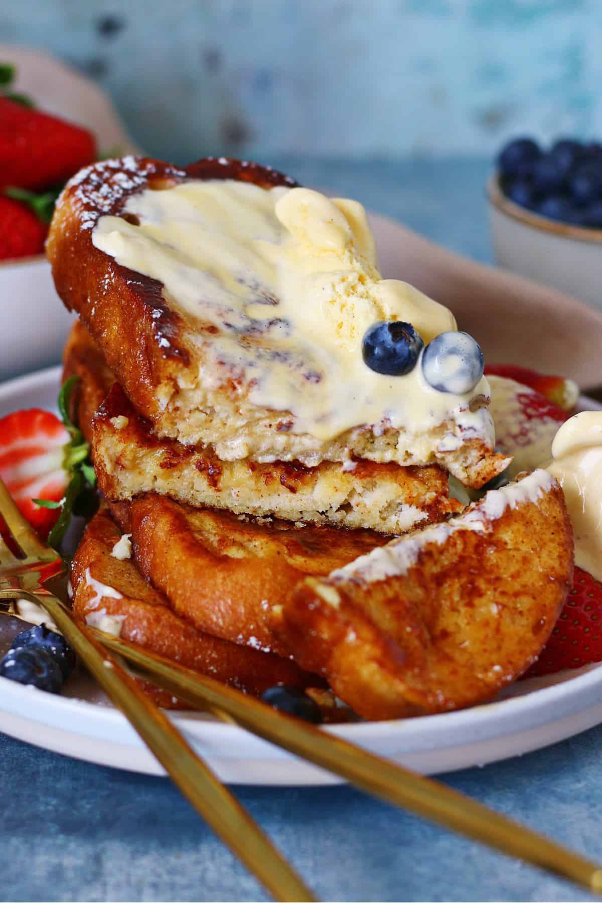 Sliced pile of heavily garnished French toast with a knife and fork on the side in a plate.
