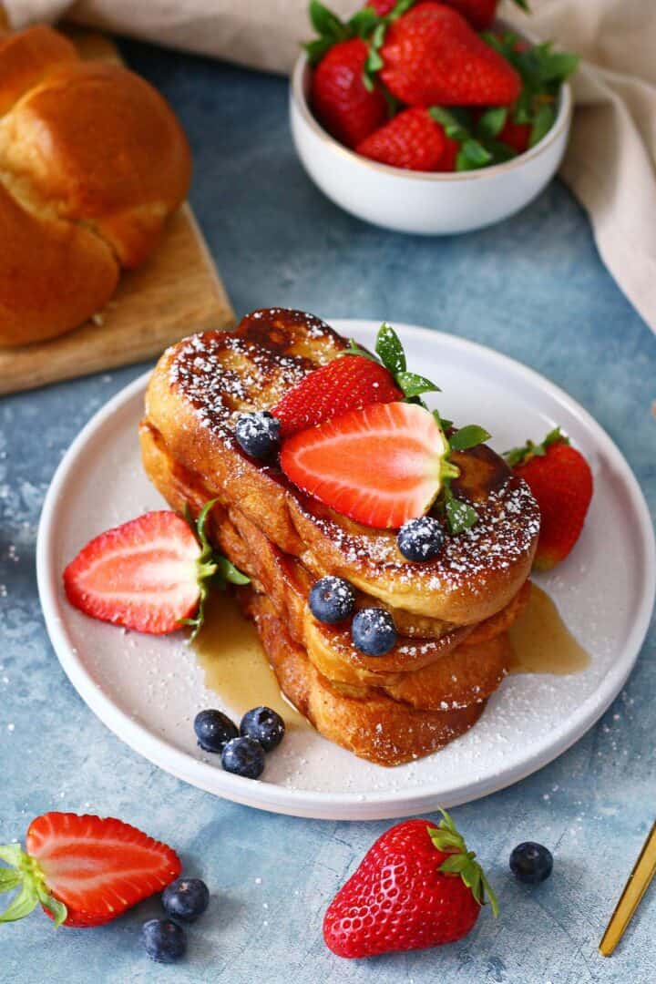 A stack of buttermilk French toast garnished with berries, powdered sugar and maple syrup.
