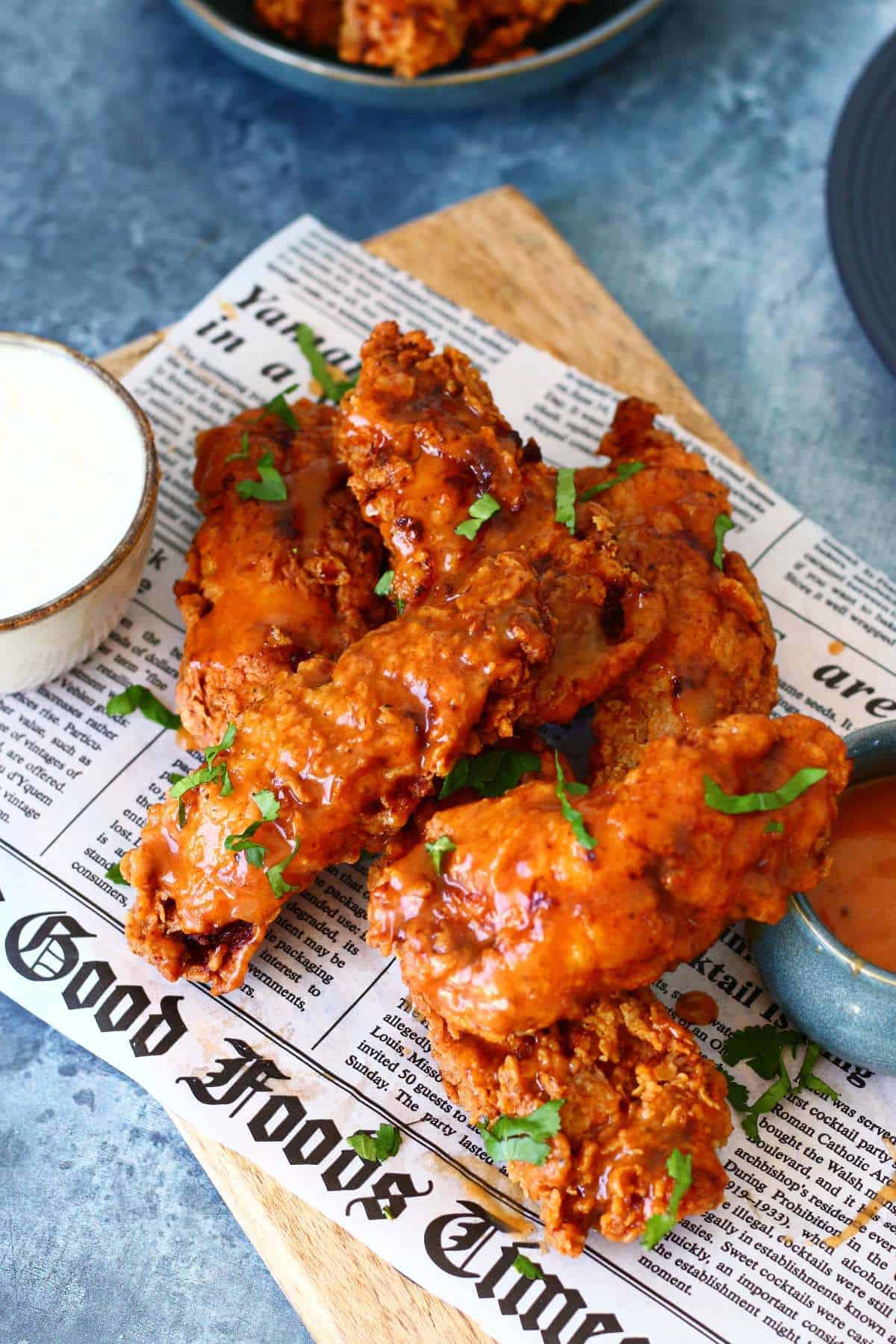 Buffalo chicken tenders with sauces and garnish on a newspaper.