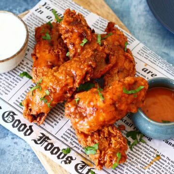 Chicken tenders with buffalo sauce and ranch dip on a newspaper.