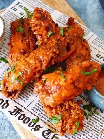 Chicken tenders with buffalo sauce and ranch dip on a newspaper.