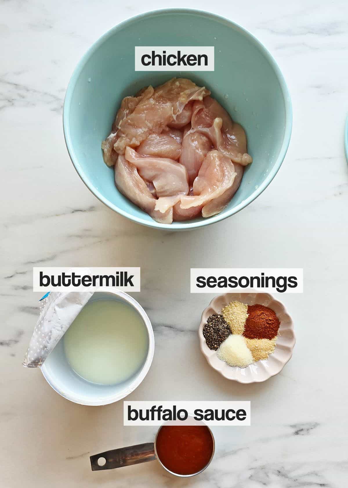 Ingredients for chicken marinade in bowls on a marble counter.