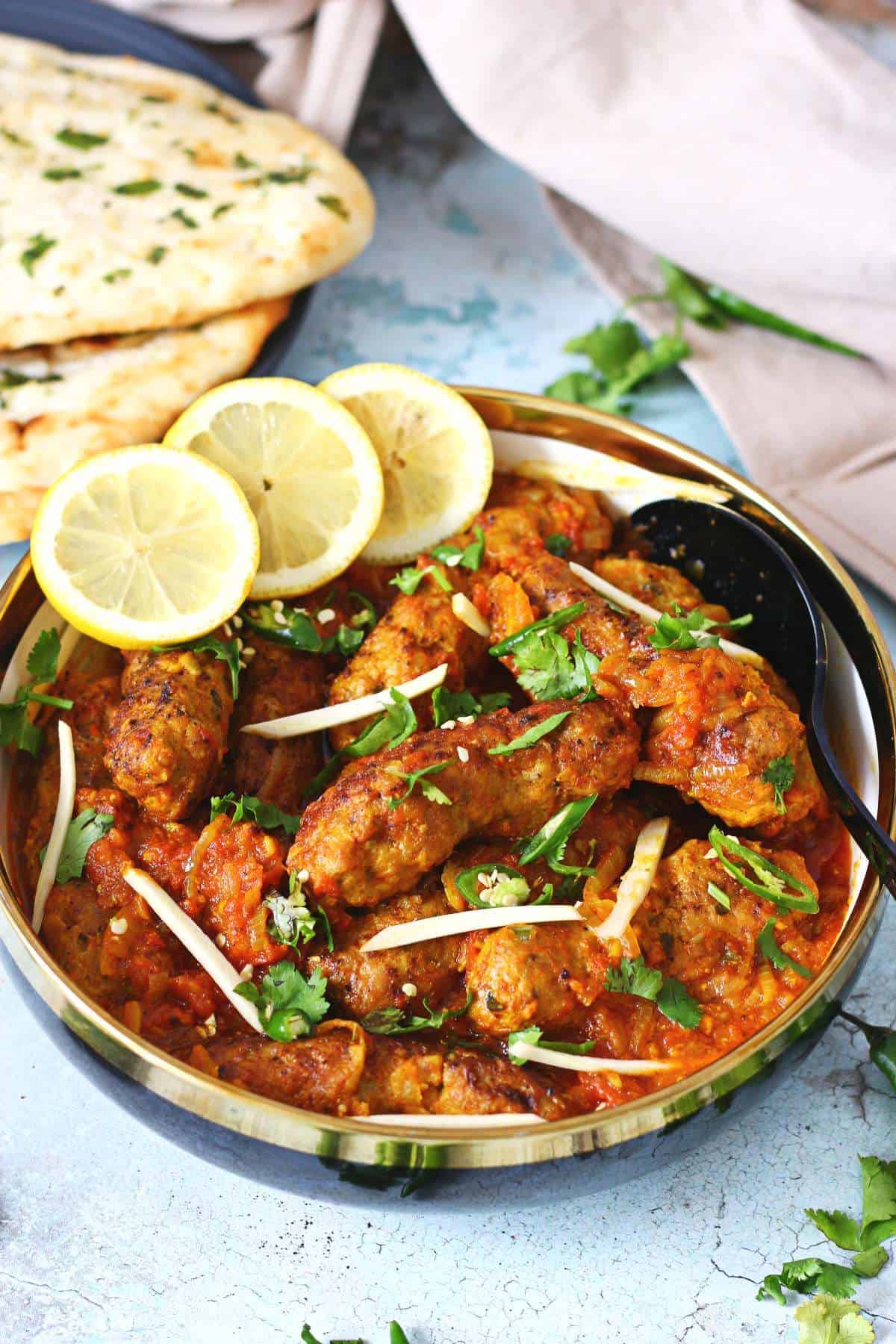 Beef kabab curry in a black serving dish with spoon on the side and garnished with lemon slices, sliced ginger and fresh cilantro.