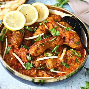 Kabab masala curry in a serving dish with lemon slices and garnishes.