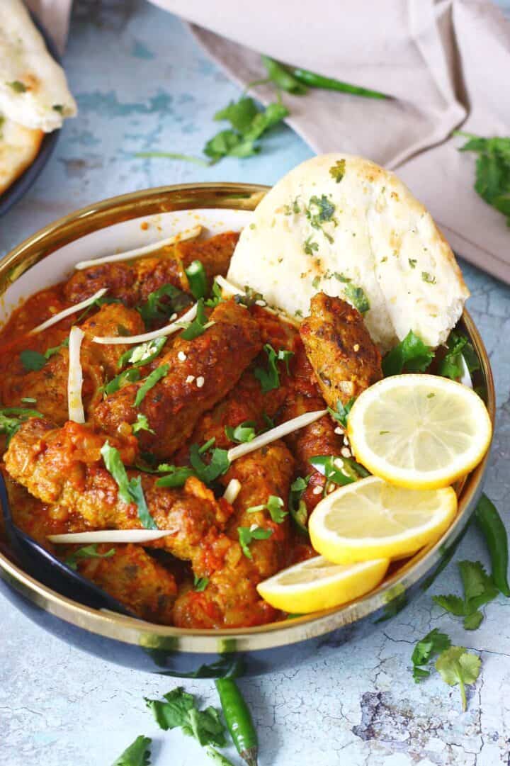 A bowl of kabab curry with lemon slices and a piece of flatbread.