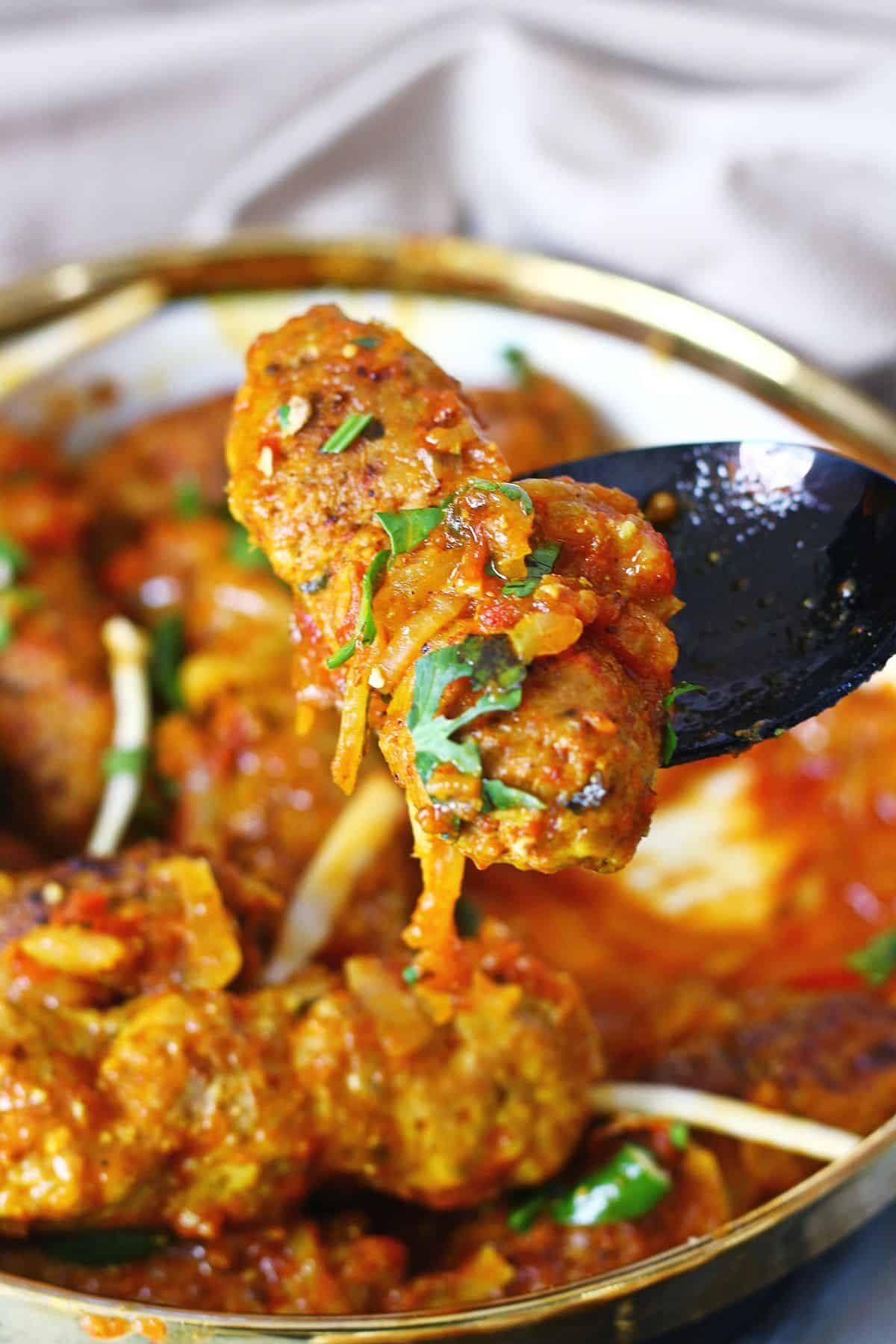 A beef kabab with curry in a black spoon.