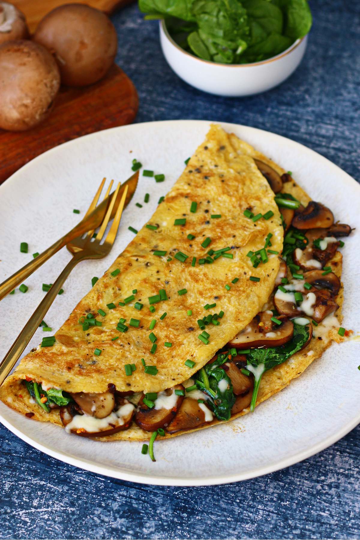 A white plate with stuffed spinach and mushroom omelette and fork and knife on the side.