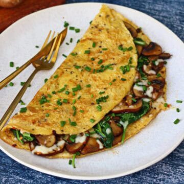Stuffed spinach and mushroom omelette garnished with chives on a white plate.