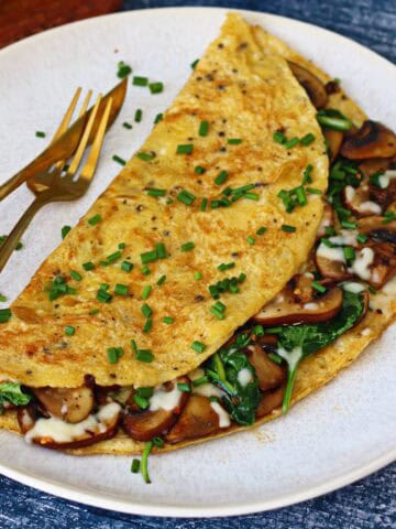 Stuffed spinach and mushroom omelette garnished with chives on a white plate.
