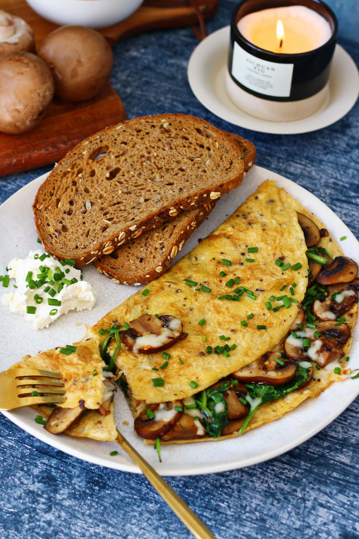 Spinach and mushroom omelette served with sliced bread and cream cheese on a white plate, with a bite of omelette on a fork.