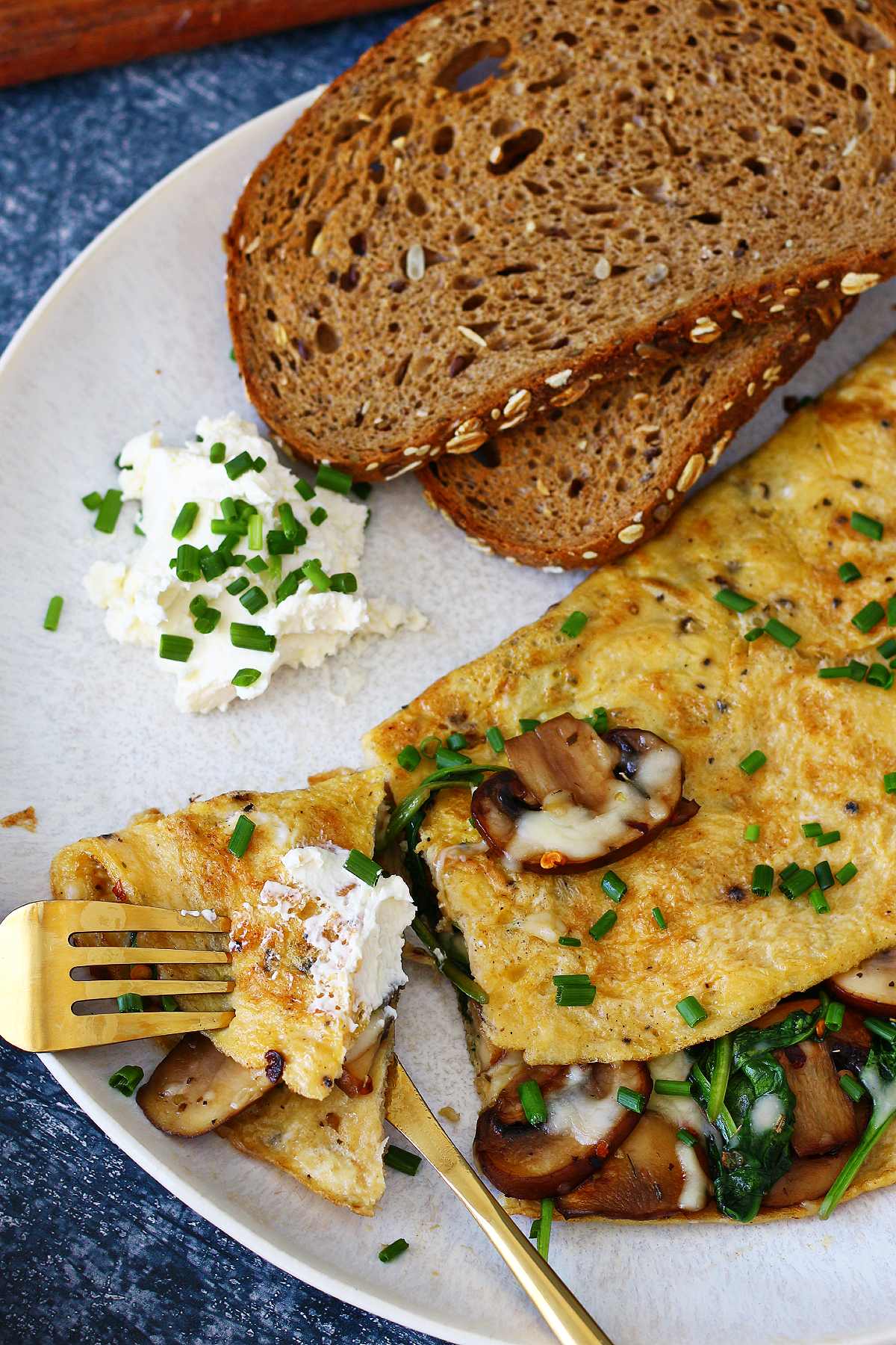 Stuffed mushroom omelette on a fork slathered with cream cheese with the rest of the omelette on the side.