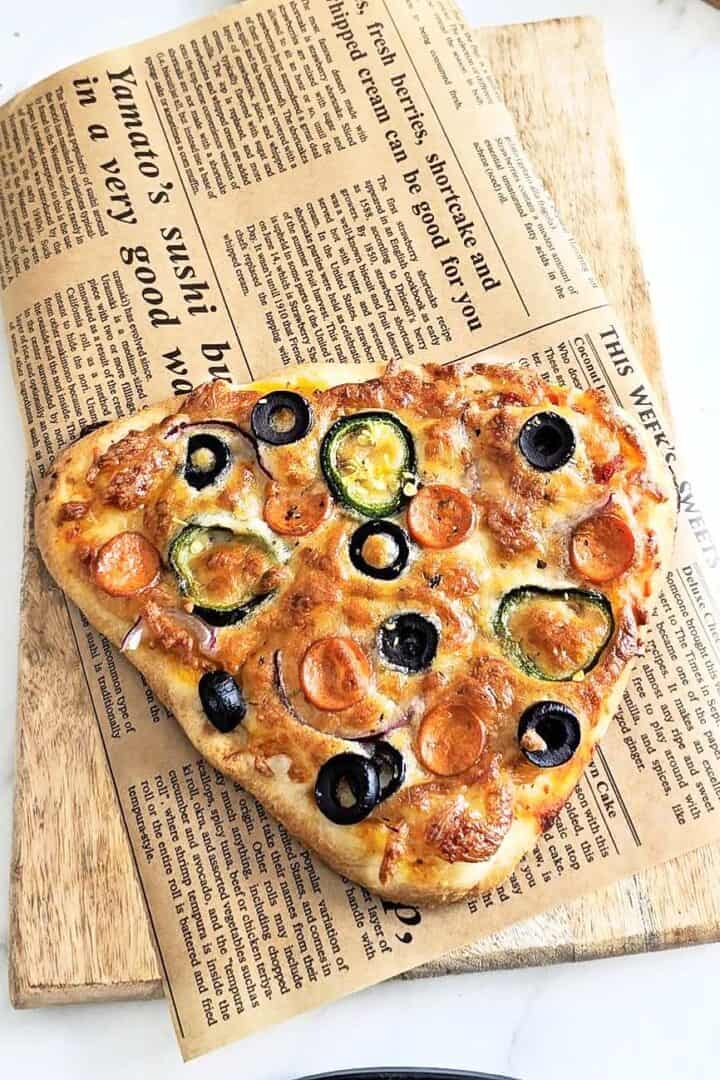 Freshly baked flatbread pizza on a baking sheet over a wooden board.