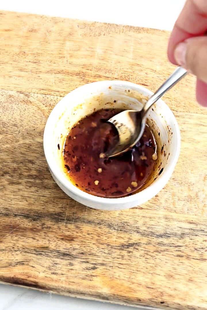 Mixing hot honey sauce in a white dip bowl over a wooden board.