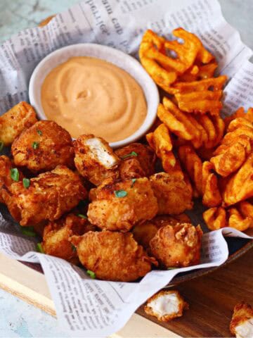 A shallow bowl lined with newspaper filled with chicken nuggets, waffle fries and chipotle dip.