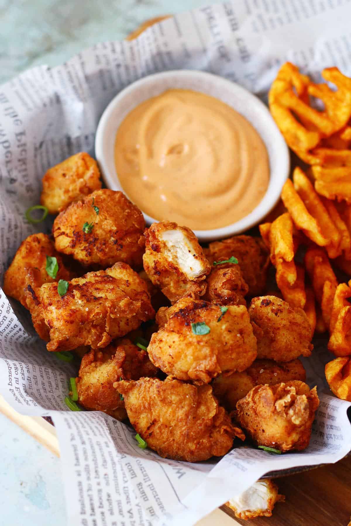 Close up of a broken piece of chicken nugget in a plate of nuggets.