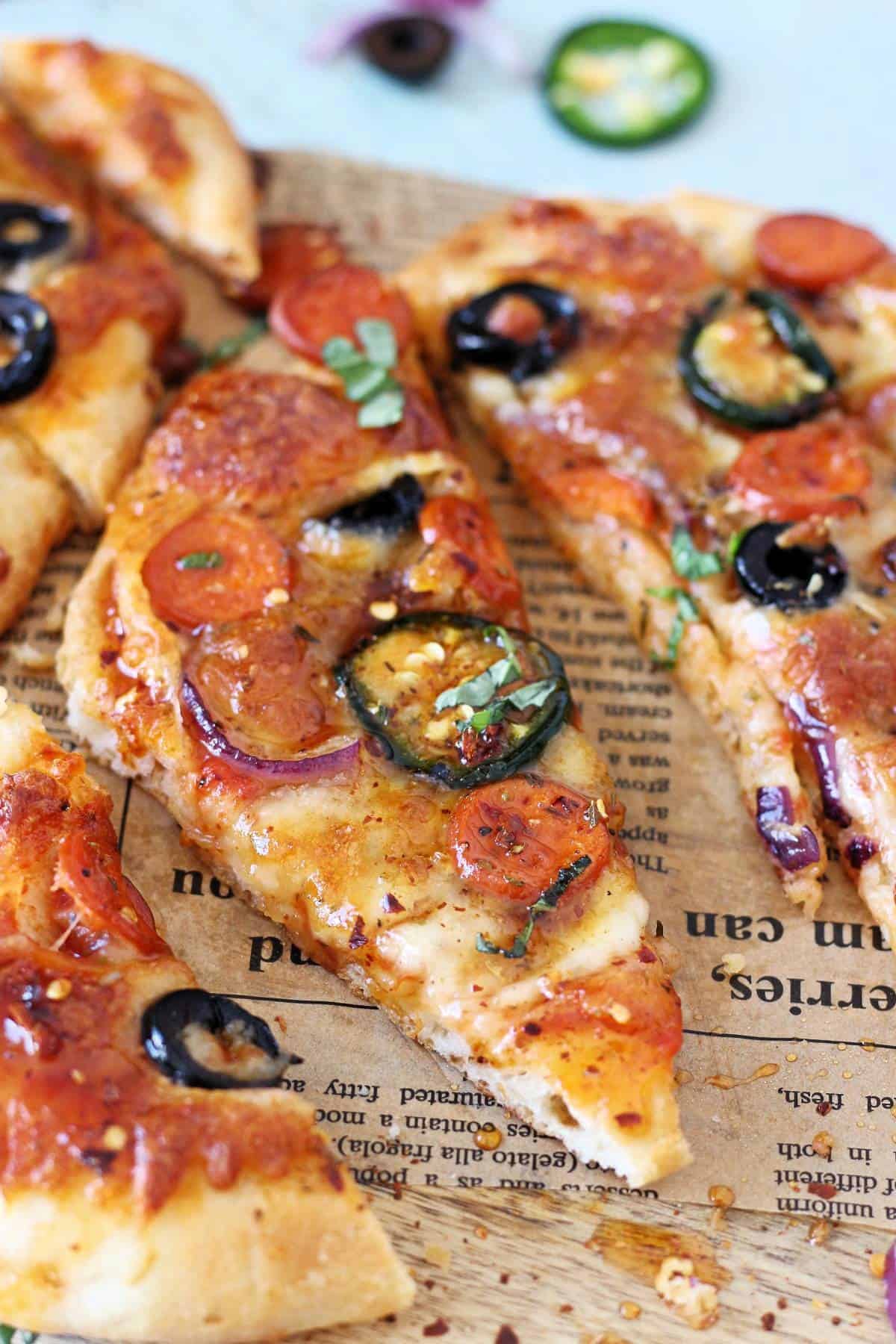 Close up of one slice of hot honey flat bread pizza topped with pepperoni, olives and jalapenos.