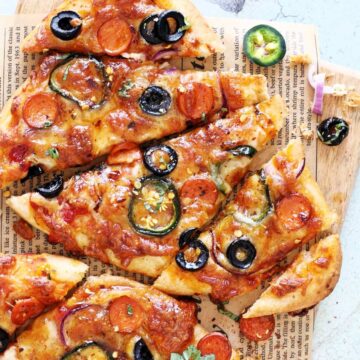 Flatbread pizza with pepperoni, black olives, and jalapenos on a wooden board.