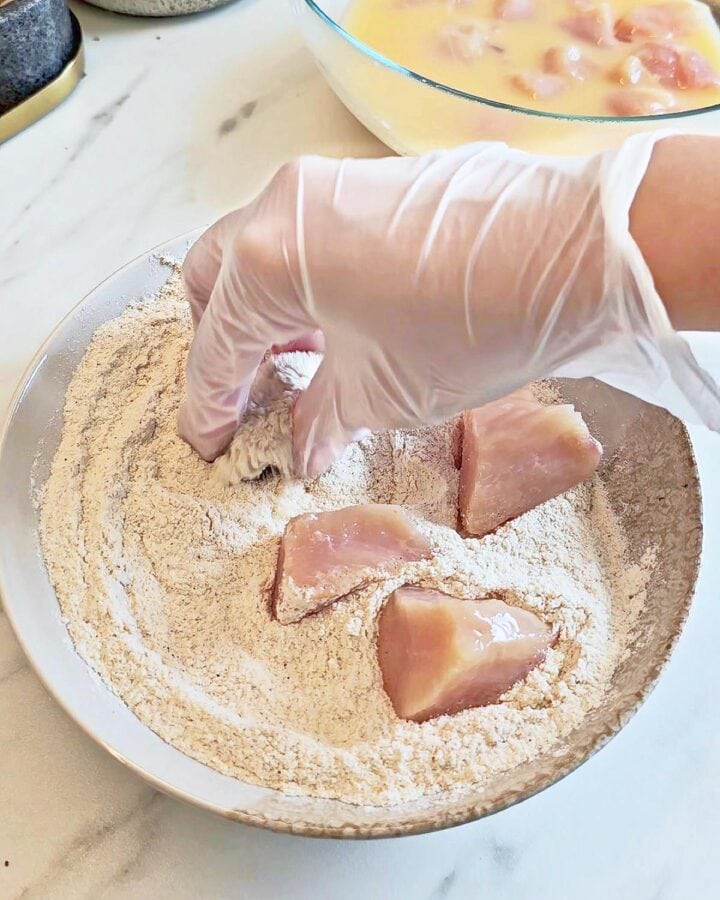 Coating raw chicken pieces with flour in a shallow plate.