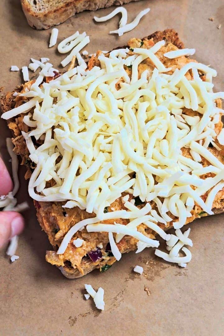 Shredded cheese on top of an open sandwich toast.