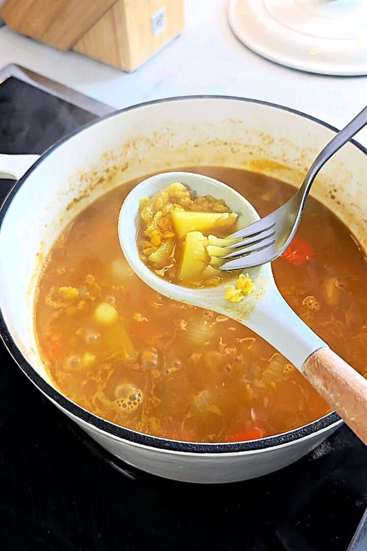 Testing the tenderness of potatoes in the soup with a fork in a ladle.