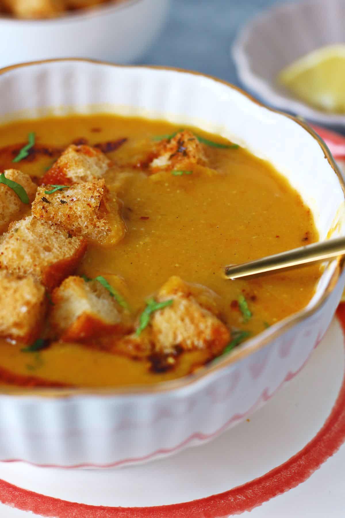 A gold spoon dipped inside a bowl of red lentil soup.
