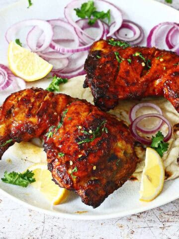 Two tandoori chicken on a plate with naan, lemon wedges and red onions.