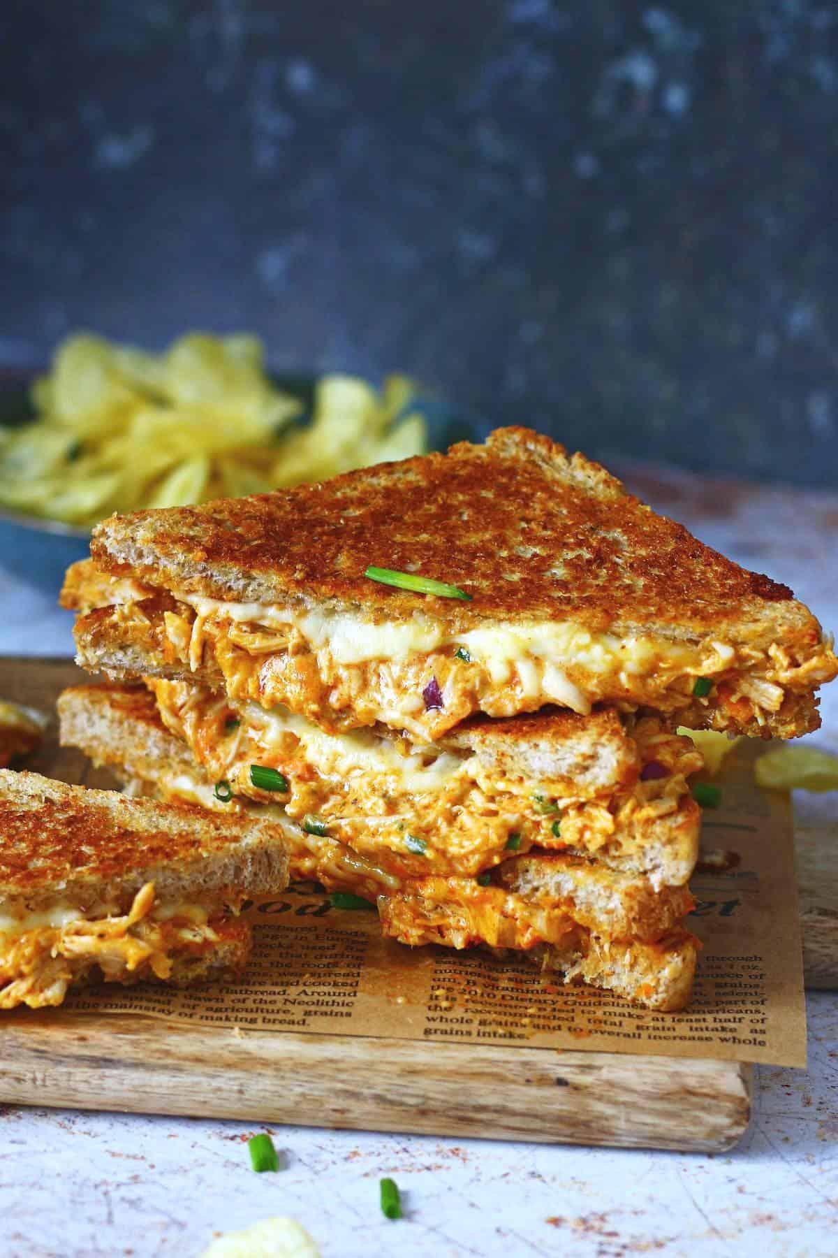 Stack of chicken melt triangles with a bowl of crisps in the background.