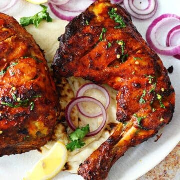 Tandoori chicken leg on a garnish of red onion rings.