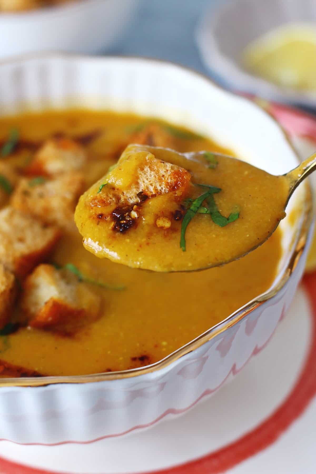 A spoonful of red lentil soup with a piece of crouton and garnishes.