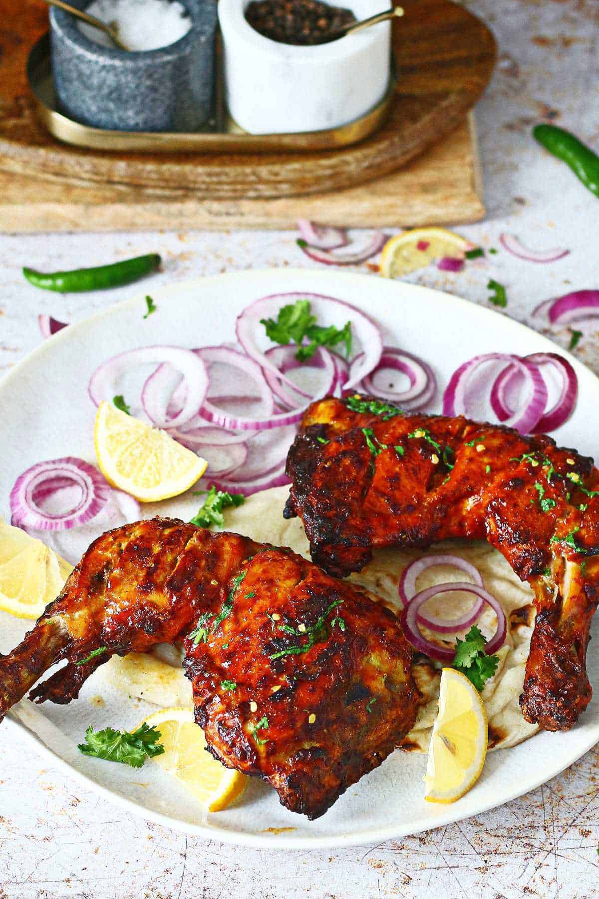 A plate of two air fryer tandoori chicken quarters served with lemon wedges, naan and sliced red onions.