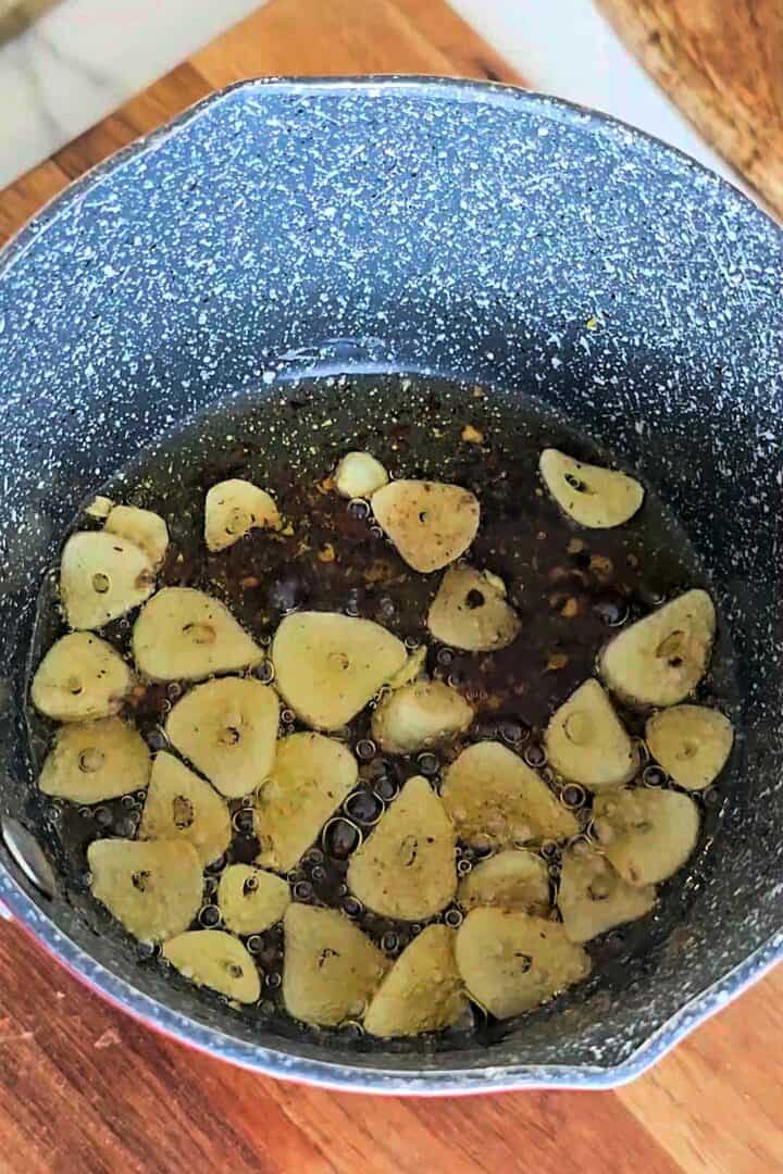 Garlic slices frying in oil in a small pot.