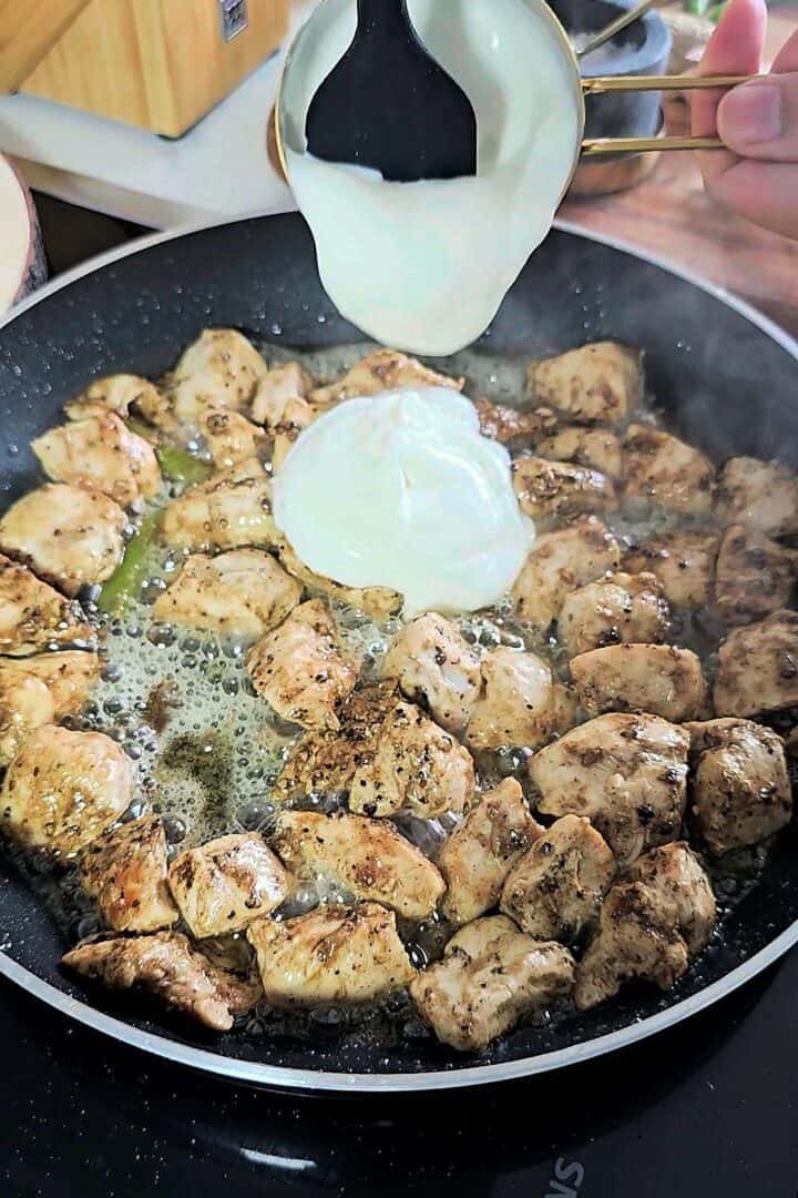 Plain yogurt being poured into the chicken and spice mixture while cooking.