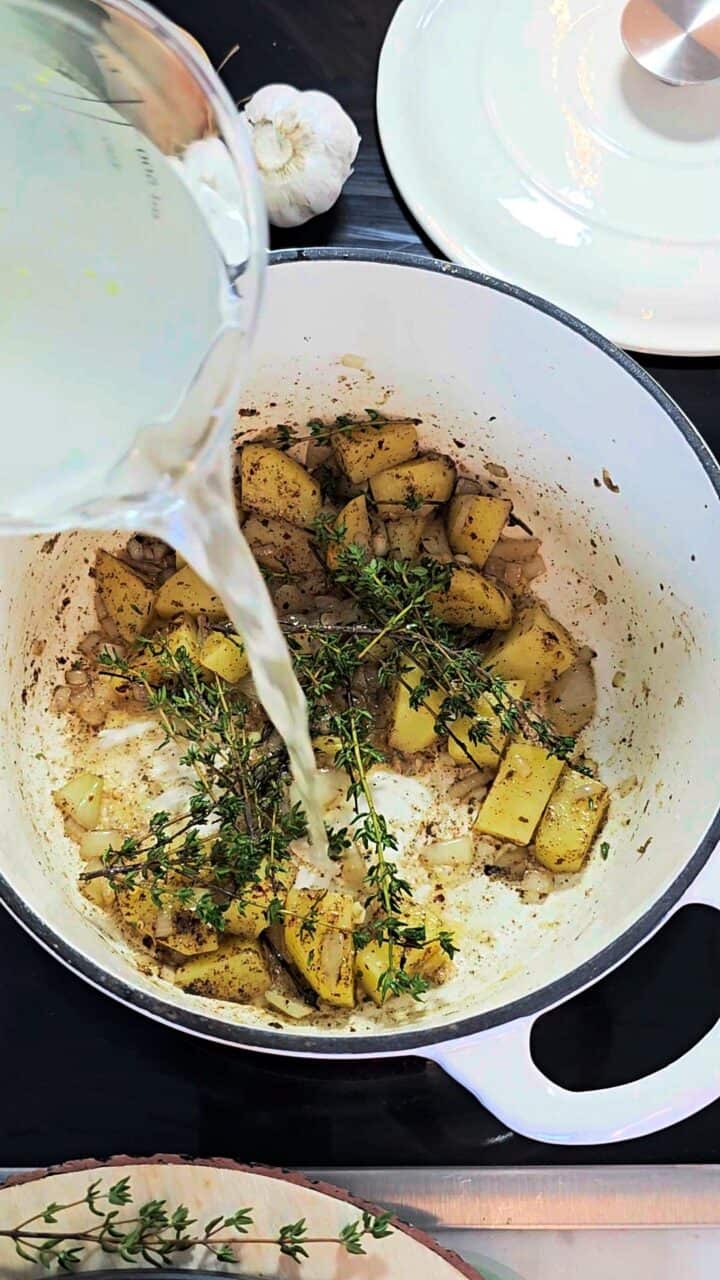 Broth being poured into a pot with potatoes and thyme sprigs.